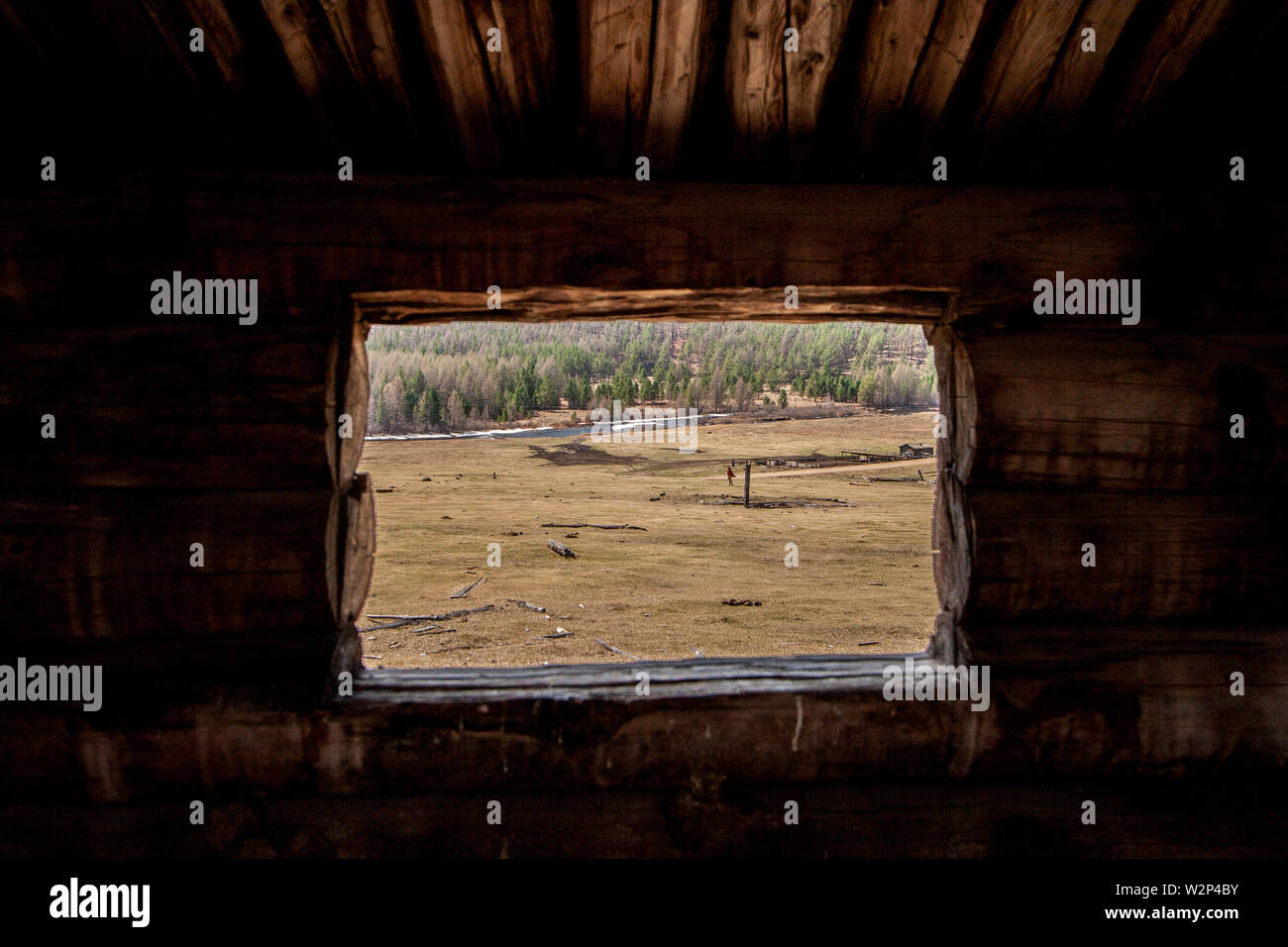 La vista dalla finestra di log al campo con una fattoria e un fiume. Telaio del log. Contro lo sfondo della foresta, sul campo di vecchi log. Un marrone Foto Stock