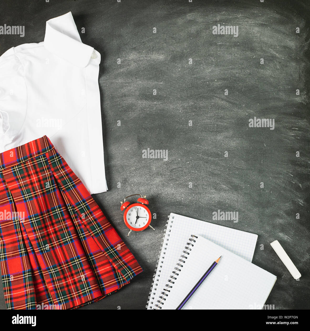 Notebook uniformi scolastiche per una ragazza shirt mantello una sveglia chalk board. Il concetto di torna a scuola e istruzione. Foto Stock