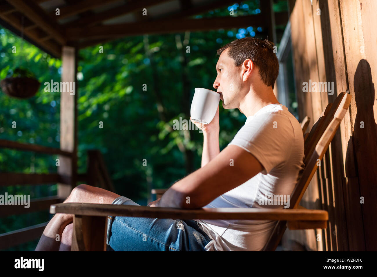 Uomo seduto in relax sulla sedia a dondolo sul portico di casa nella  mattina di cabina in legno cottage di bere il caffè da cup Foto stock -  Alamy