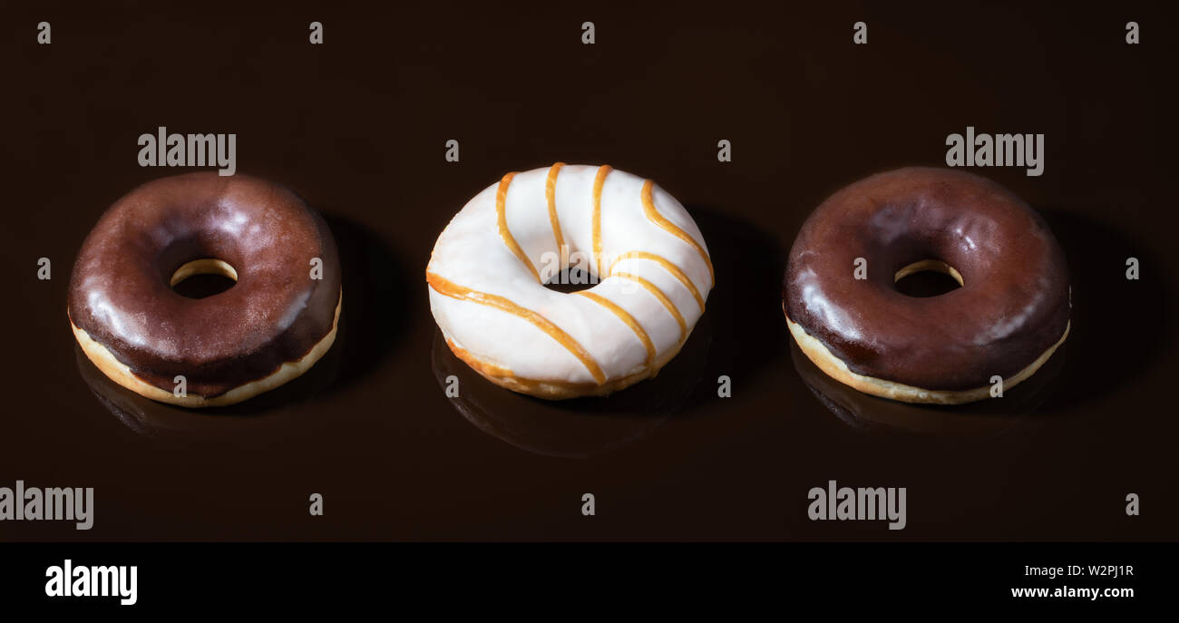 Tre ciambelle vetrate sul cioccolato fondente al fondo liscio. Foto Stock