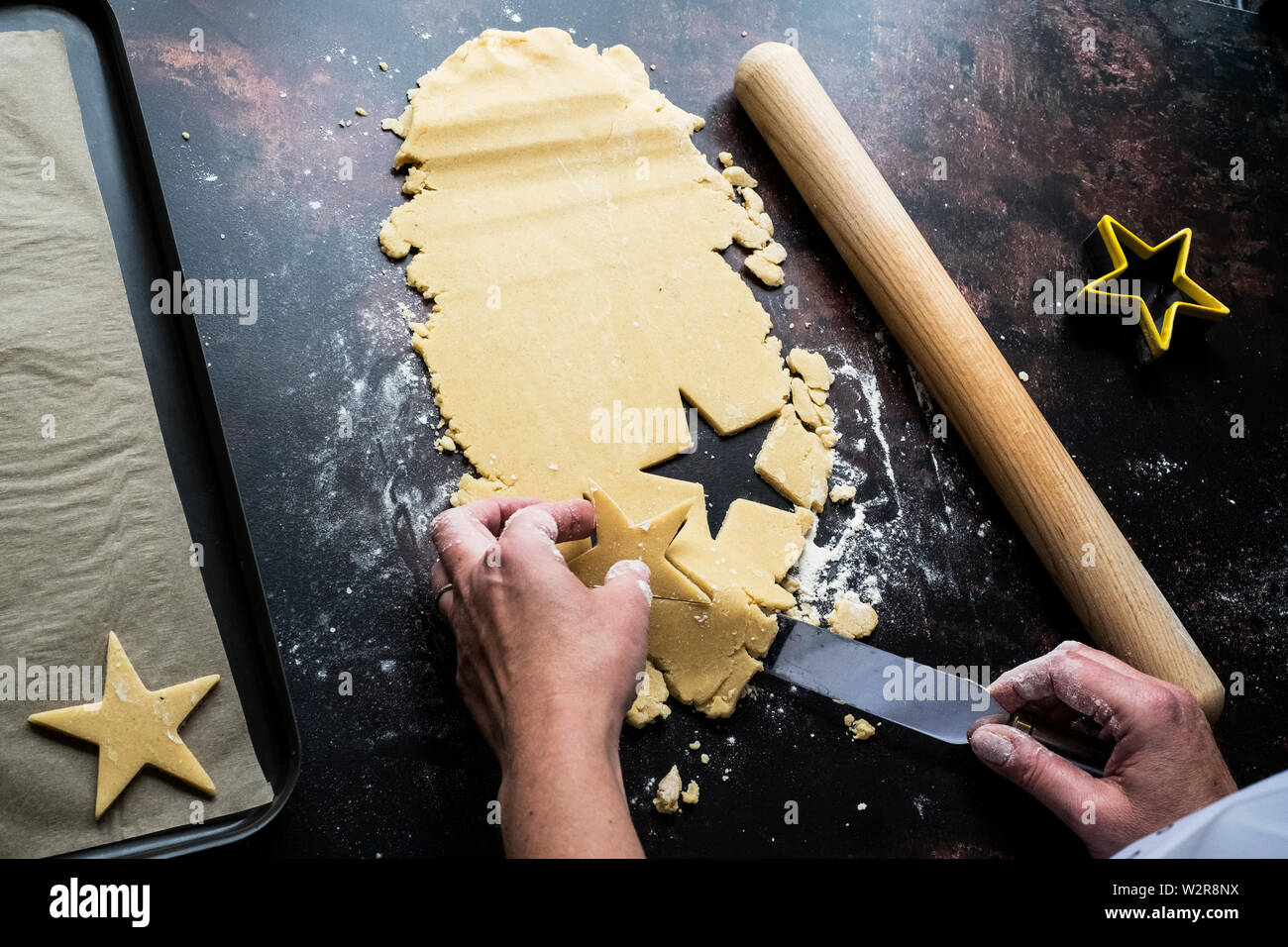 Angolo alto close up di persona il sollevamento tagliati a forma di stella i cookie su un vassoio da forno con una tavolozza coltello. Foto Stock