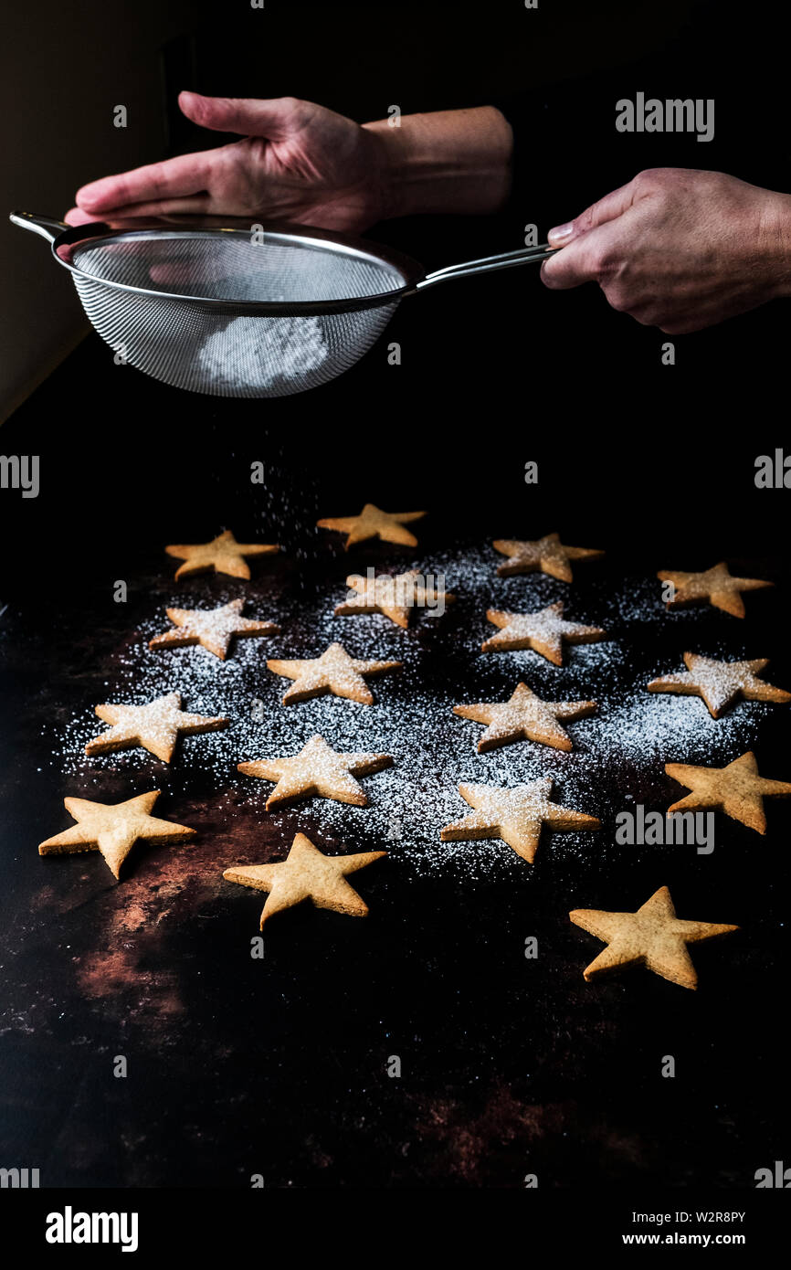 Angolo alto close up della persona spolvero fresco cotto al forno a forma di stella i biscotti con zucchero a velo. Foto Stock