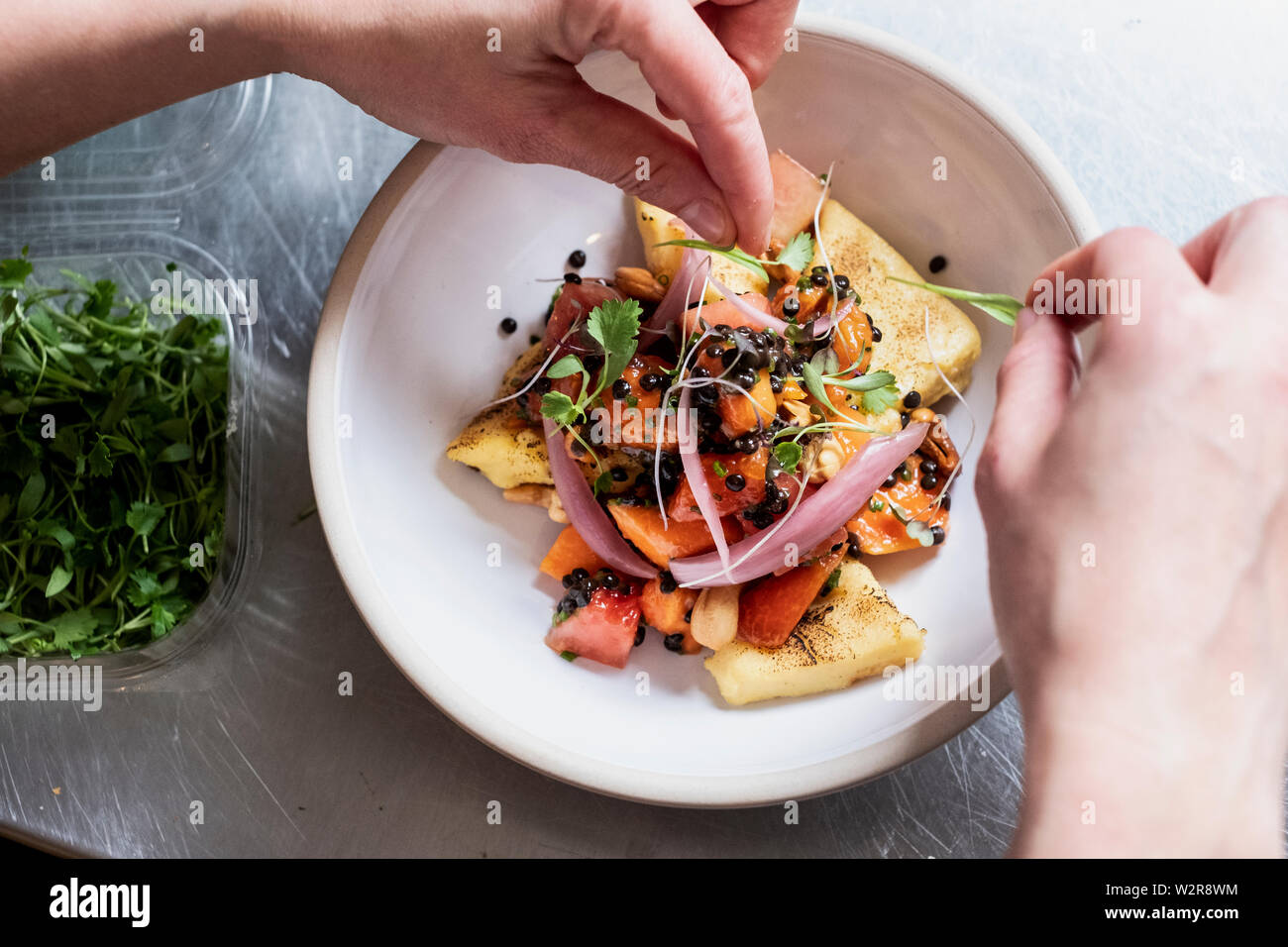 Angolo alto close up di persona la piastra di farcitura di prodotti alimentari con alcune erbe. Foto Stock