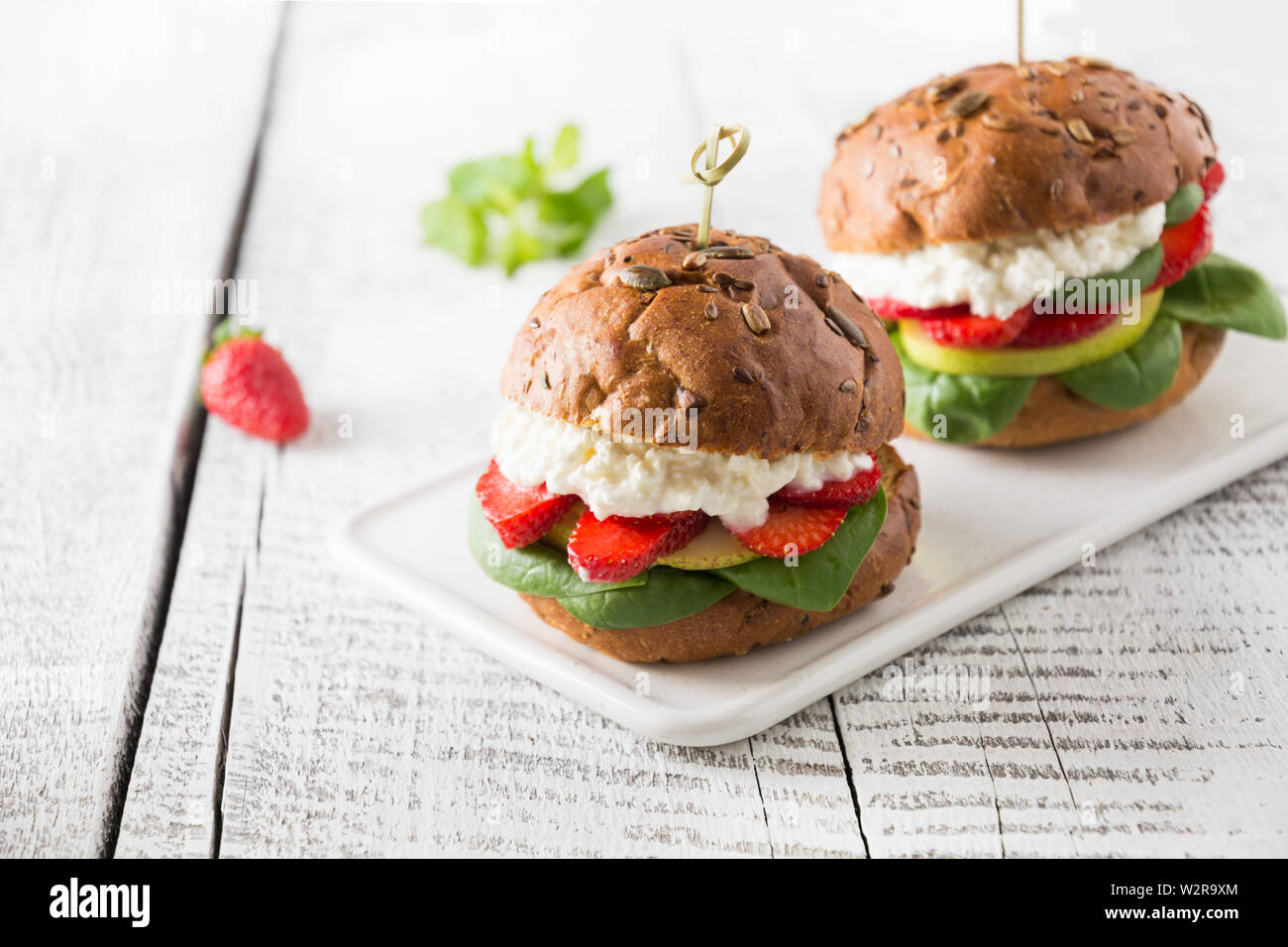 Vegan burger con fragola, pera, ricotta e spinaci freschi sul panino con semi di zucca bianco sulla tavola di legno. Spazio per il testo. Foto Stock