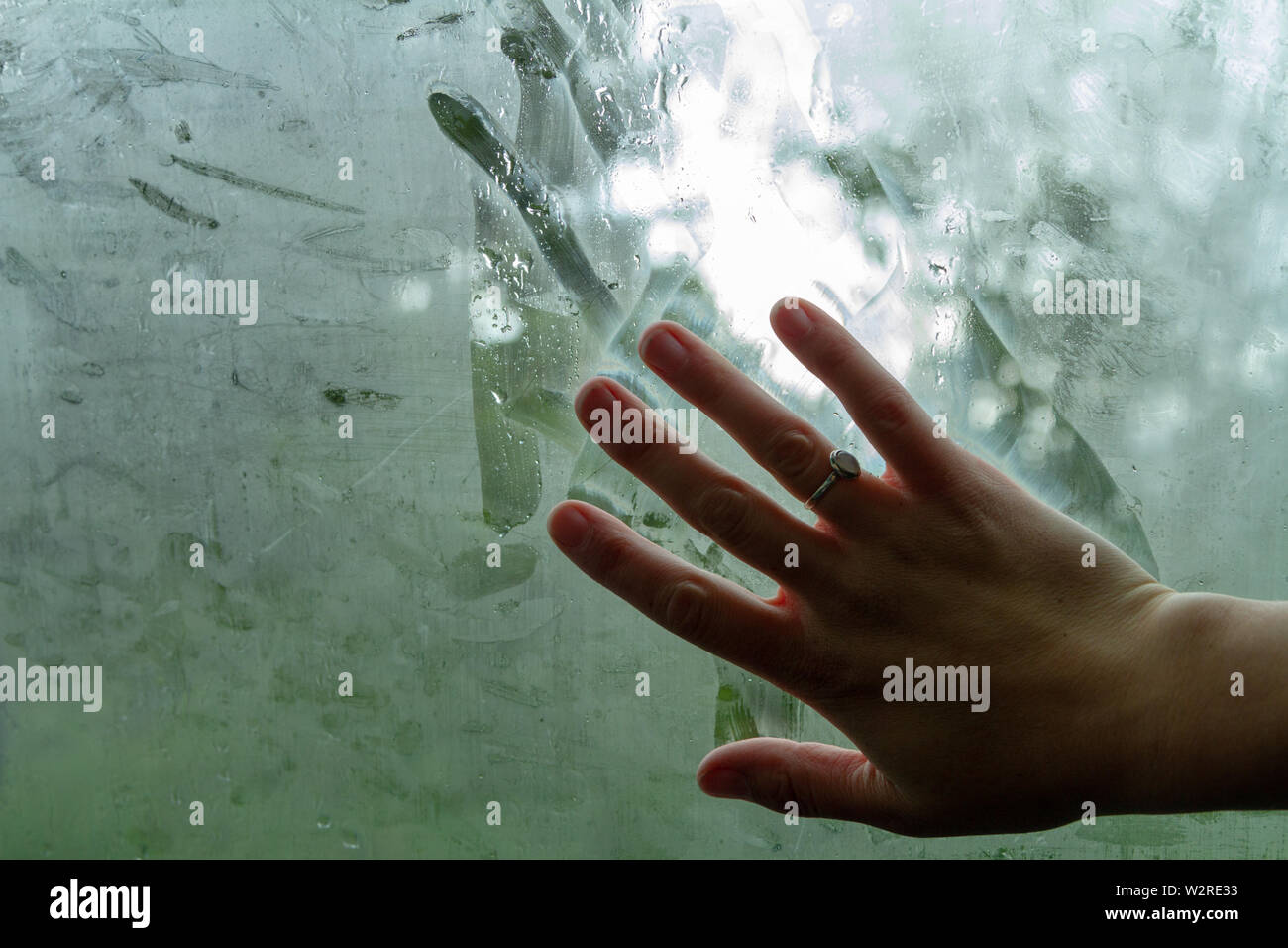 Femmina trascinando la mano e le dita lasciando striature su una finestra steamy in un umido auto. Foto Stock