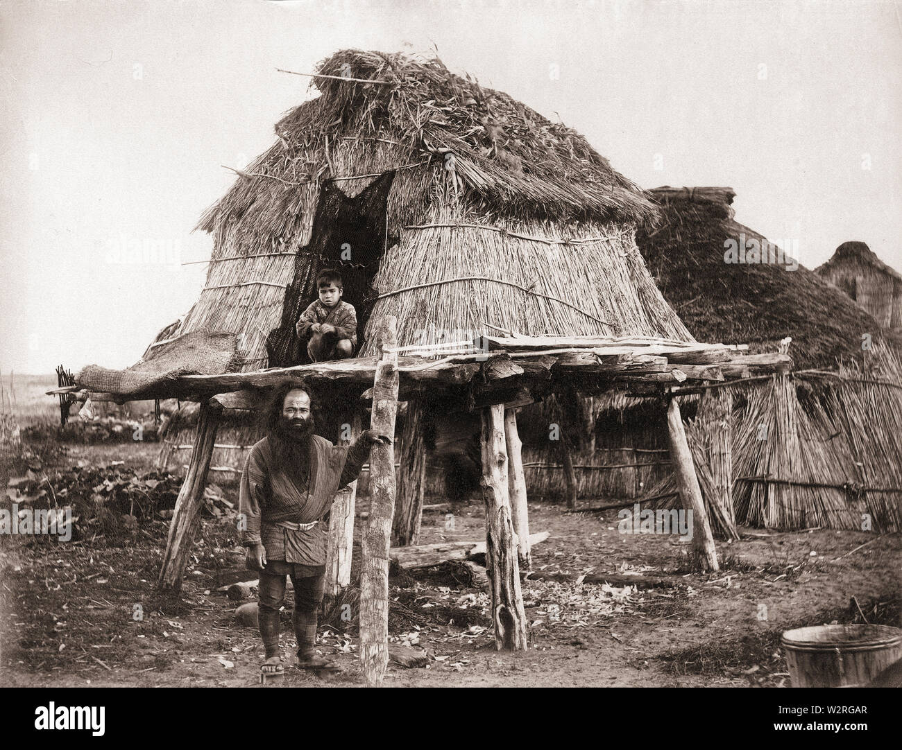 [ 1870 Giappone - Ainu Storehouse, Hokkaido ] - Ainu un uomo e suo figlio al di fuori di una struttura sopraelevata noto come 'pu' in cui il cibo e le disposizioni sono state memorizzate. Hokkaido. Xix secolo albume vintage fotografia. Foto Stock