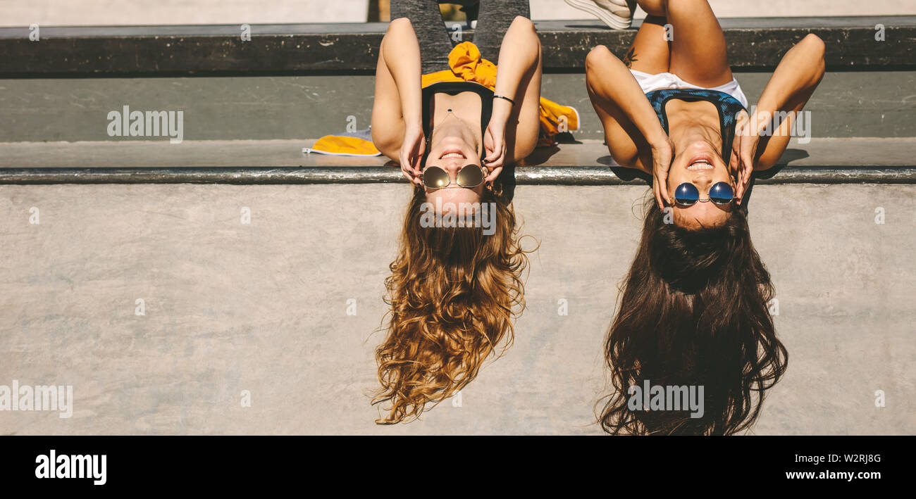 Due ragazze eleganti sdraiato a skate park con occhiali da sole. Amici di sesso femminile avente il divertimento a skate park su un giorno d'estate. Foto Stock