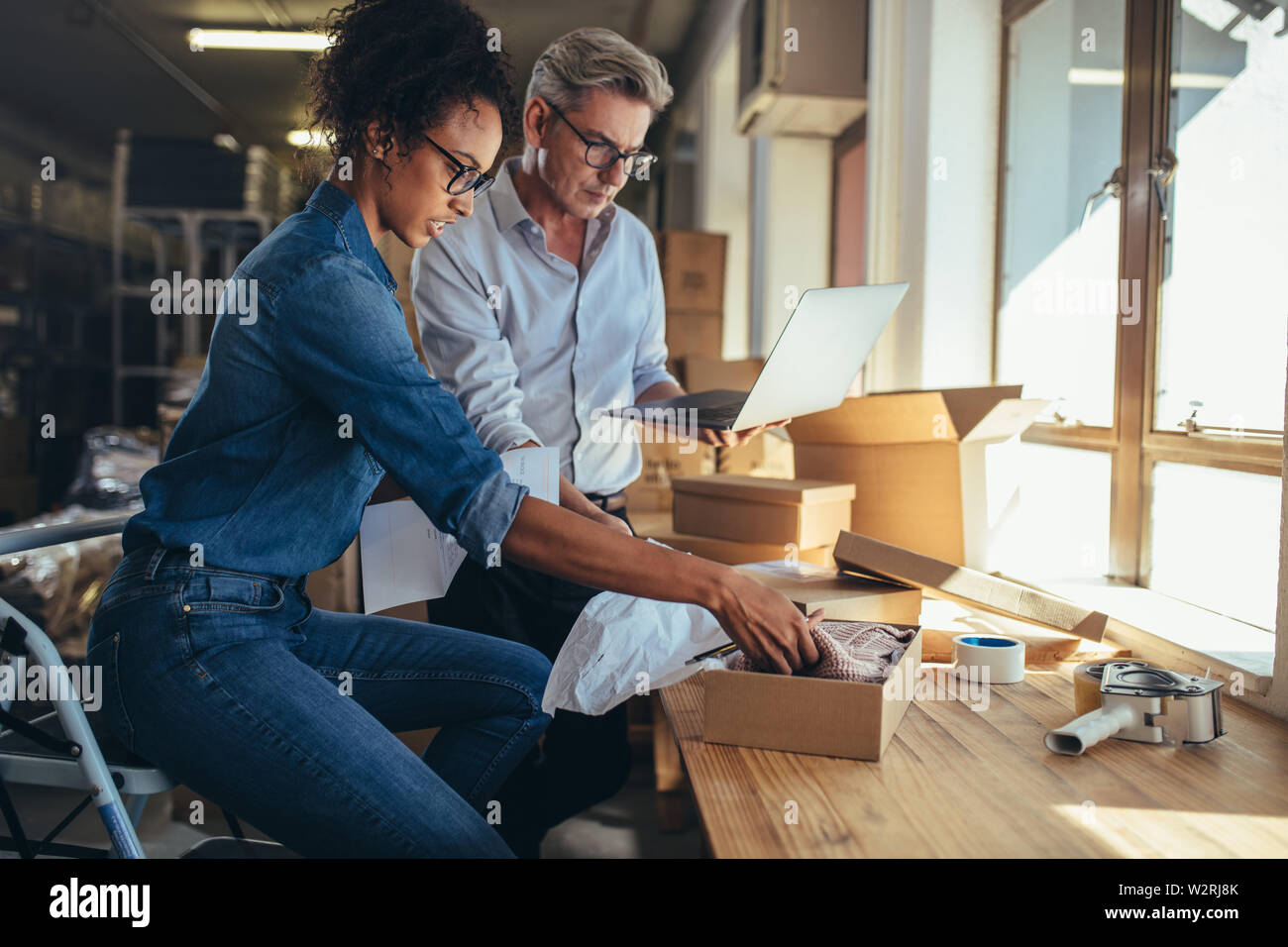 Negozio online partners la preparazione di un pacco per la spedizione. Donna di imballare il prodotto in scatola con uomo che lavora sul computer portatile. Foto Stock