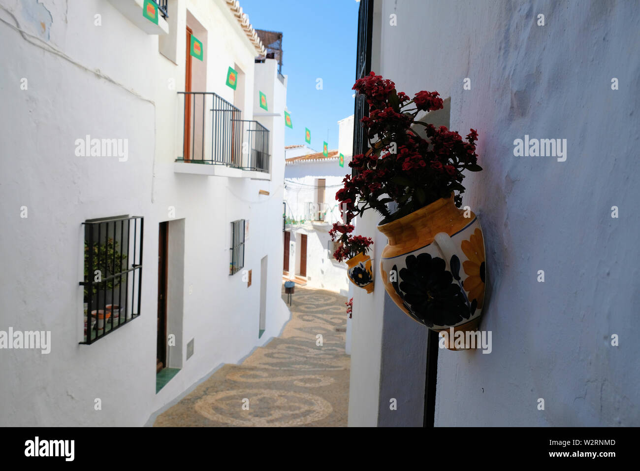 Pittoresco e pittoresca strada in Frigiliana, provincia di Malaga, Spagna; pareti dipinte di bianco con una decorazione ceramica vasi di argilla e fiori. Foto Stock