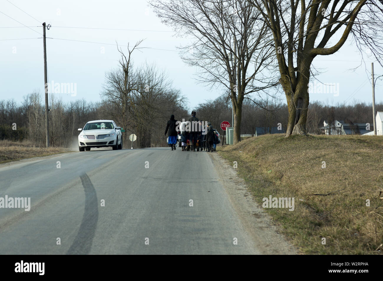 Una famiglia Amish passeggiate lungo una strada di campagna in una fredda giornata invernale vicino Spencerville, Indiana, Stati Uniti d'America. Foto Stock