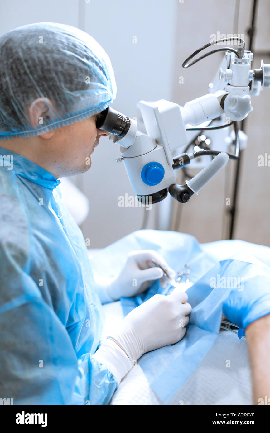 Oculista chirurgo guardando attraverso il microscopio chirurgico facendo operazione difficoltosa. Foto Stock