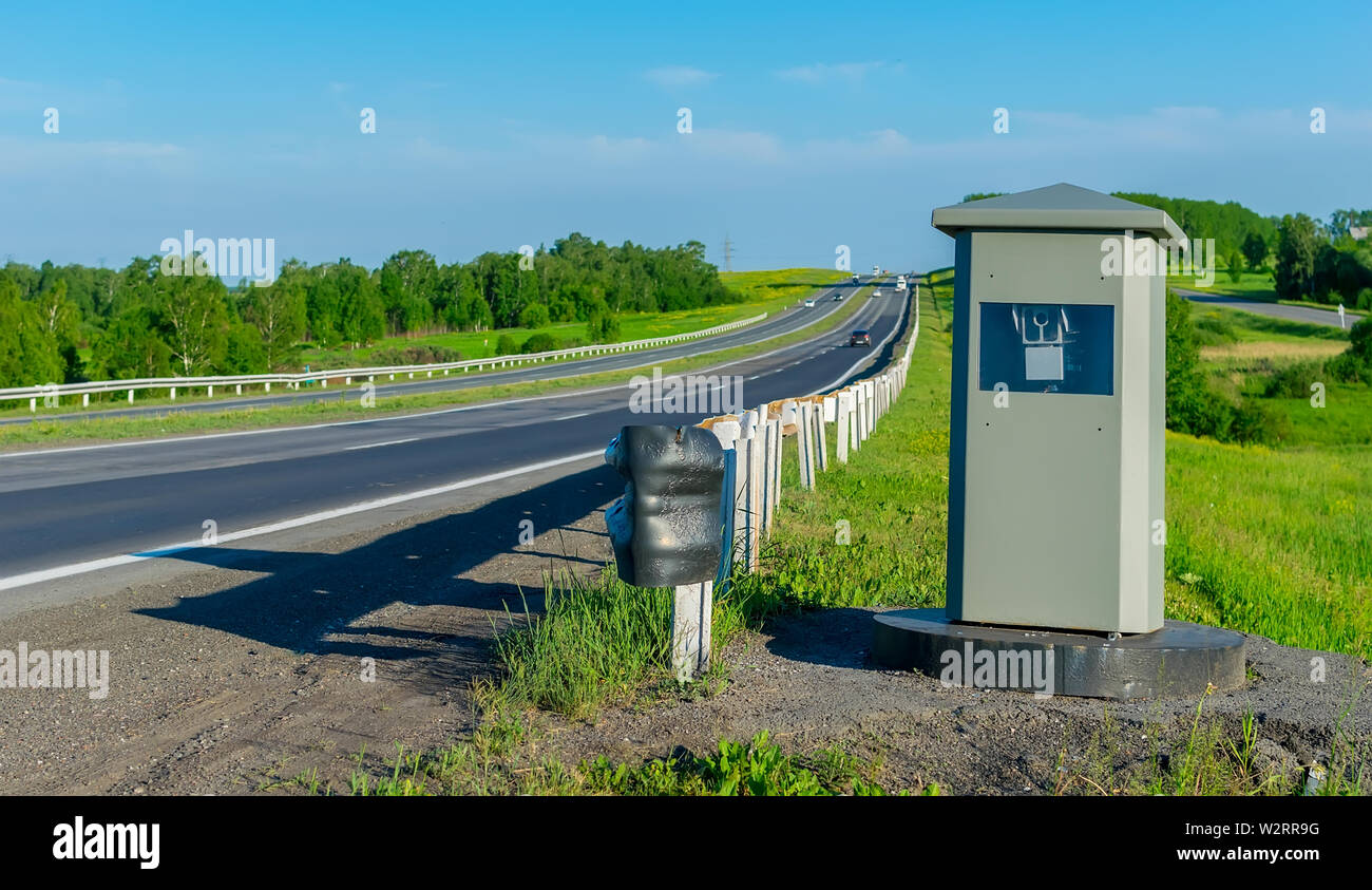Visualizza fotocamera che fissa il movimento delle vetture dal velocizzare, che sorge su una strada di campagna in estate sullo sfondo di veicoli in transito Foto Stock