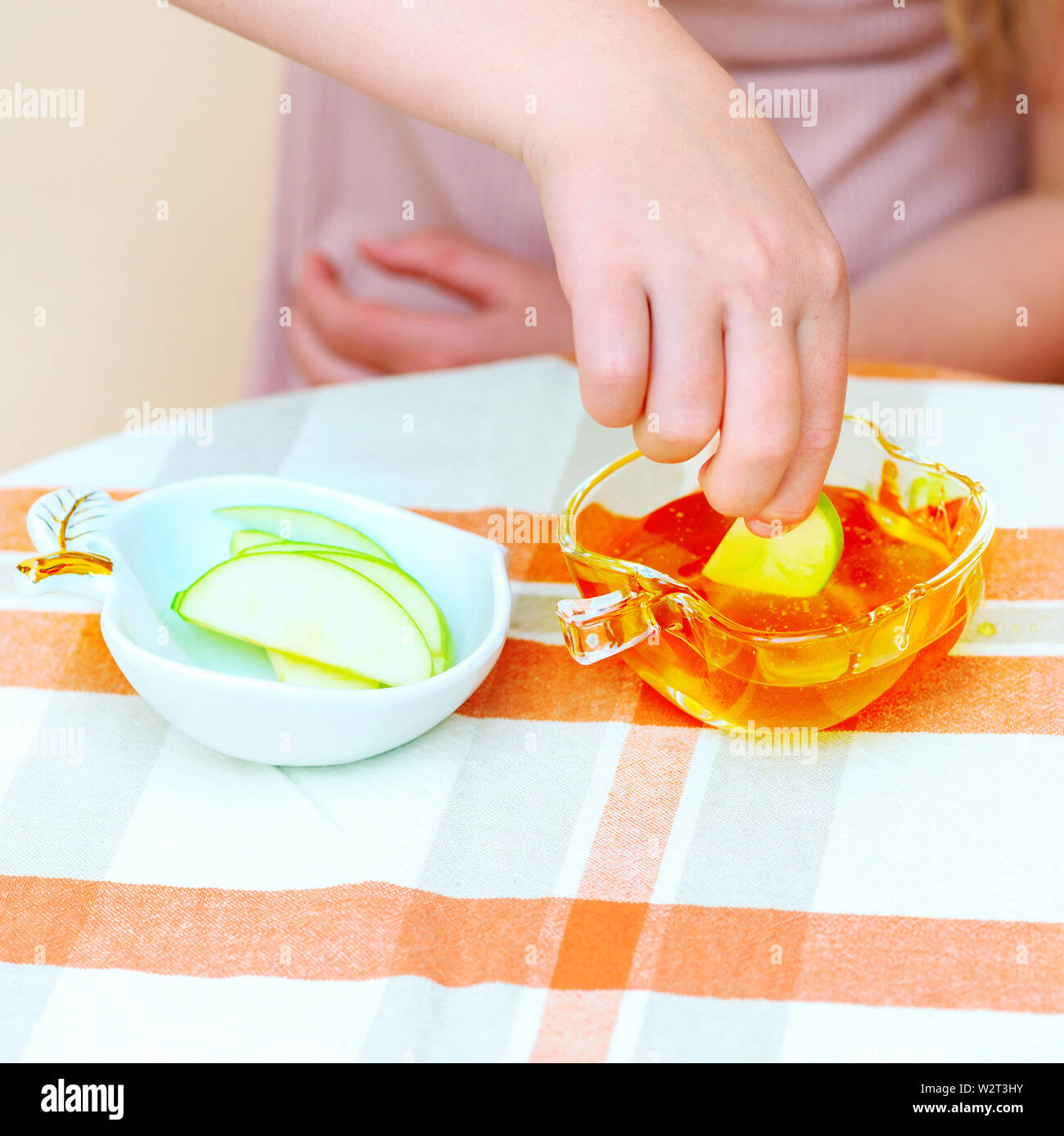 Close up di mani bambina eat apple con miele indoor. Bambino ebreo dipping fette di mela in miele su Rosh Hashanah'anno ebraico. Foto Stock