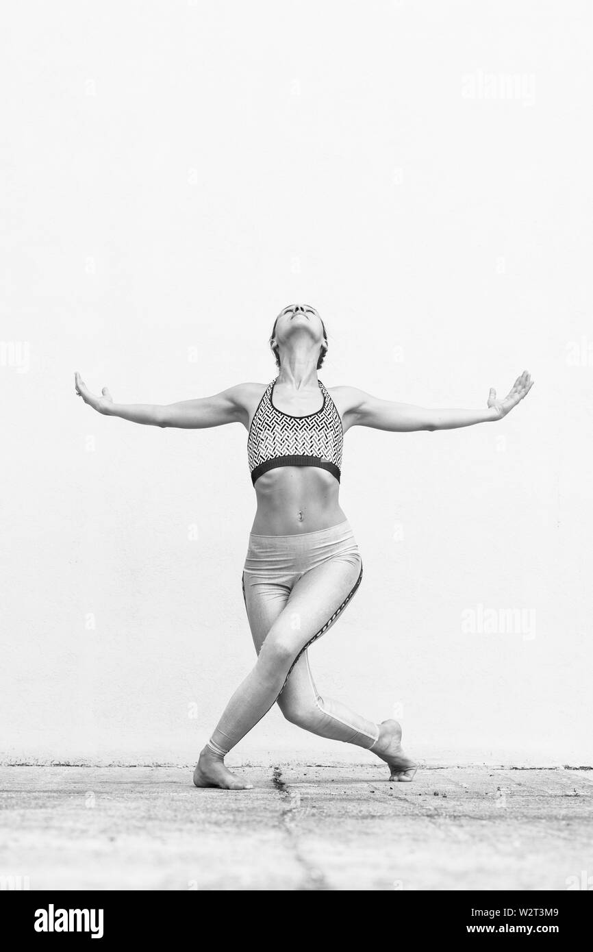 Montare sportivo ragazza attiva in sportswear facendo yoga esercizio di fitness nella parte anteriore del muro grigio, sport all'aperto, in stile urbano. Foto in bianco e nero. Foto Stock