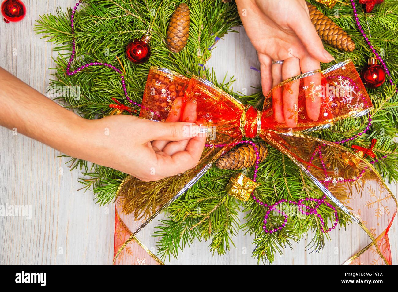 Fioraio fa una ghirlanda di Natale di rami di abete. Vista dall'alto di mani femminili. Lay piatto. Decorazione a nastro Foto Stock
