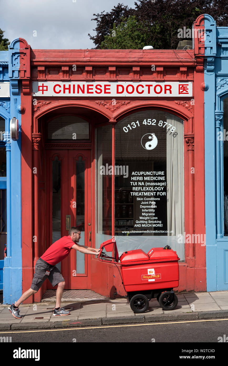 Un postino spingendo il suo carrello di mail in salita il passato medico cinese su Morningside Road, Edimburgo, Scozia, Regno Unito. Foto Stock