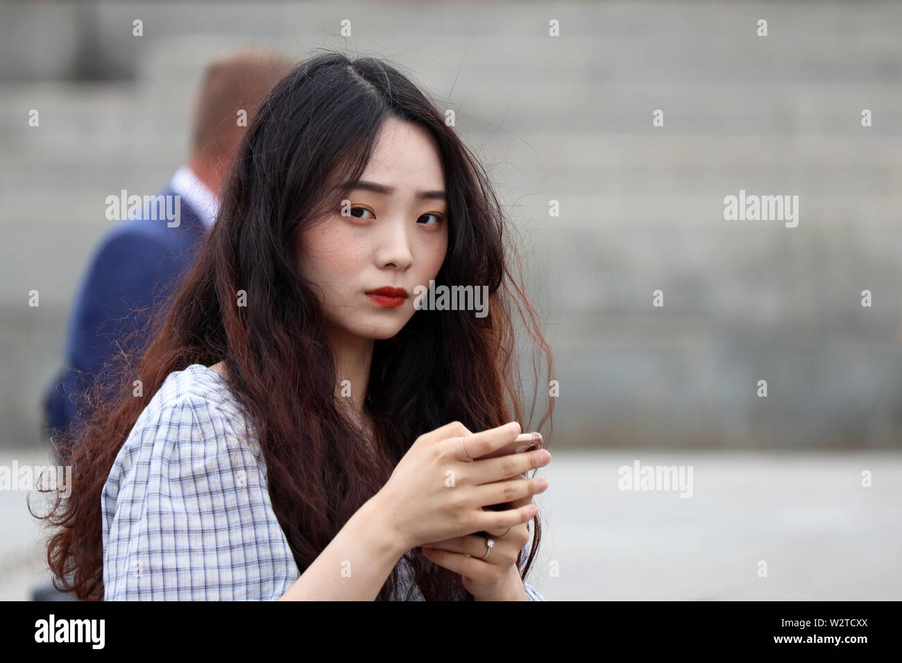 Bella ragazza asiatica con doll face in piedi su una strada di città con uno smartphone. Carino donna giovane con perfetto trucco, turistico in Russia Foto Stock