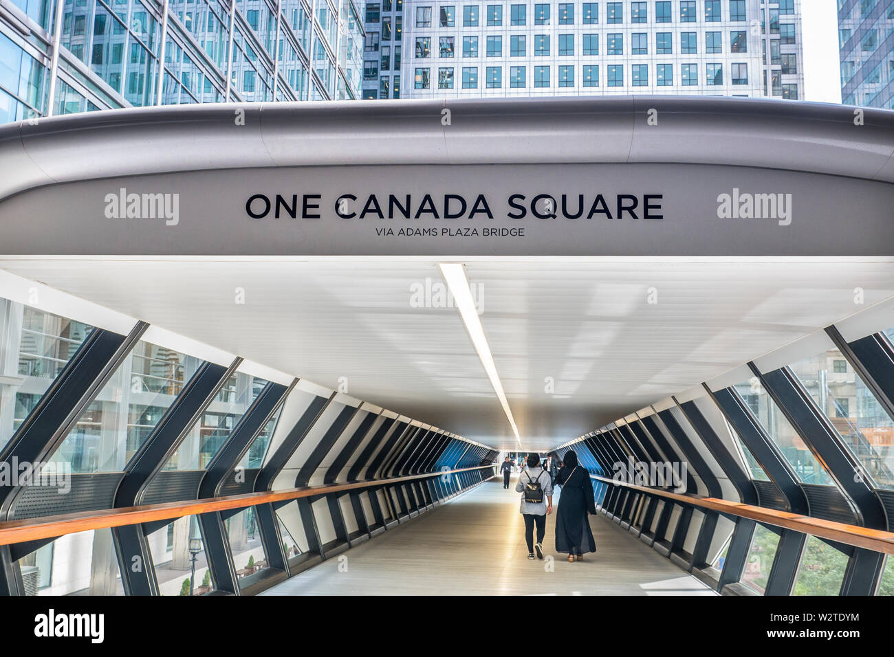 Attraversate Rail Place Adams Plaza Bridge Canary Wharf che conduce all'iconica Torre di Piazza del Canada con donne che lavorano negli uffici della Citta' che attraversano. Canary Wharf London E14 Foto Stock