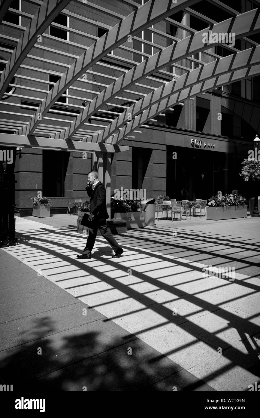 Un business man in una tuta passeggiate sotto le ombre proiettate da un sovraccarico sul tetto della struttura a reticolo in EQT Plaza, centro di Pittsburgh, Pennsylvania, USA. b&W Foto Stock