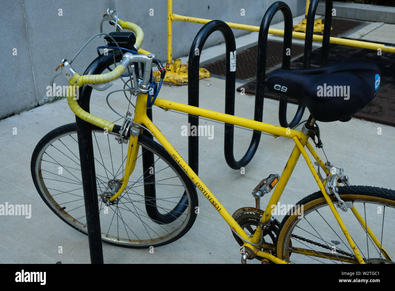 Un giallo bicicletta Schwinn è incatenato ad un nero, curva portabicicletta Foto Stock