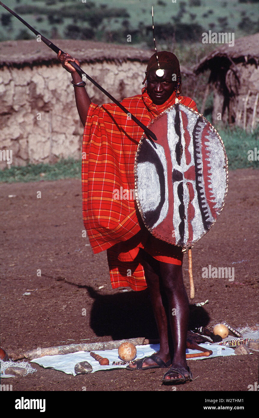 Masai warrion in full regalia di lancia e di scudo di buffalo su una manyatta vicino Sekenani Gate, Masai Mara, Kenya Foto Stock