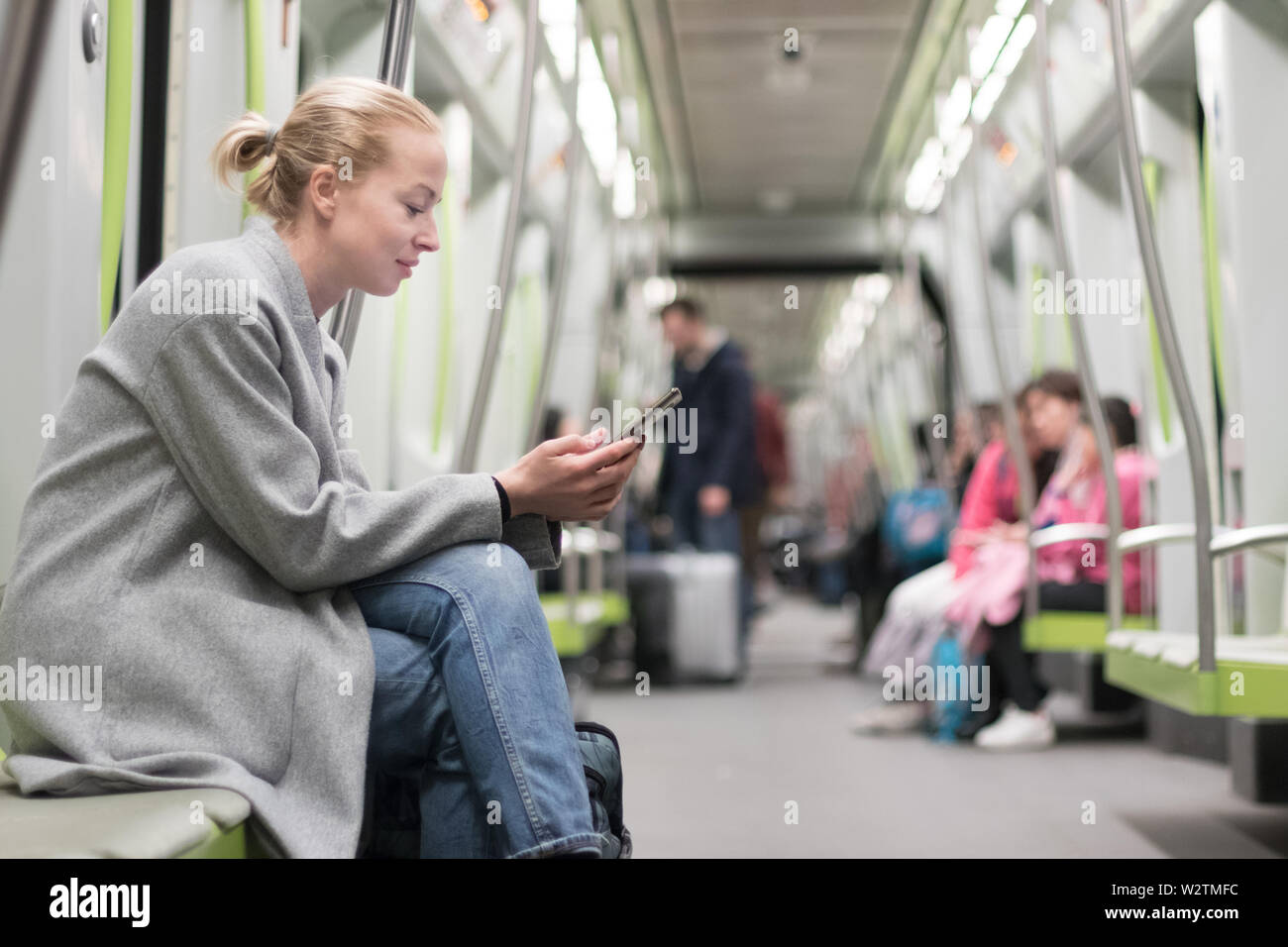 Bella donna bionda che indossa cappotto invernale la lettura al telefono mentre si è in viaggio in metropolitana dei trasporti pubblici. Foto Stock