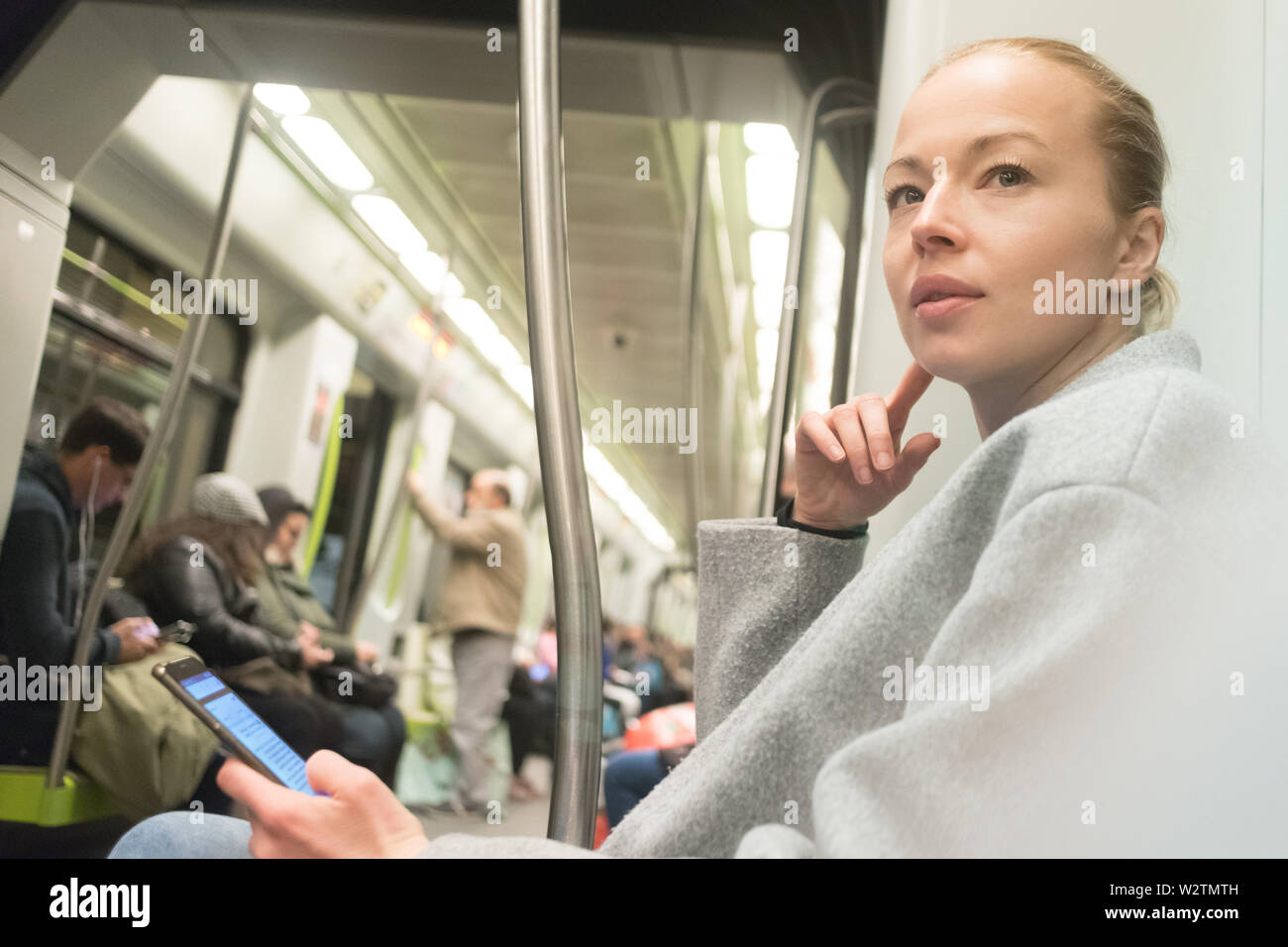 Bella donna bionda utilizzando smart phone durante il viaggio in metropolitana dei trasporti pubblici. Foto Stock