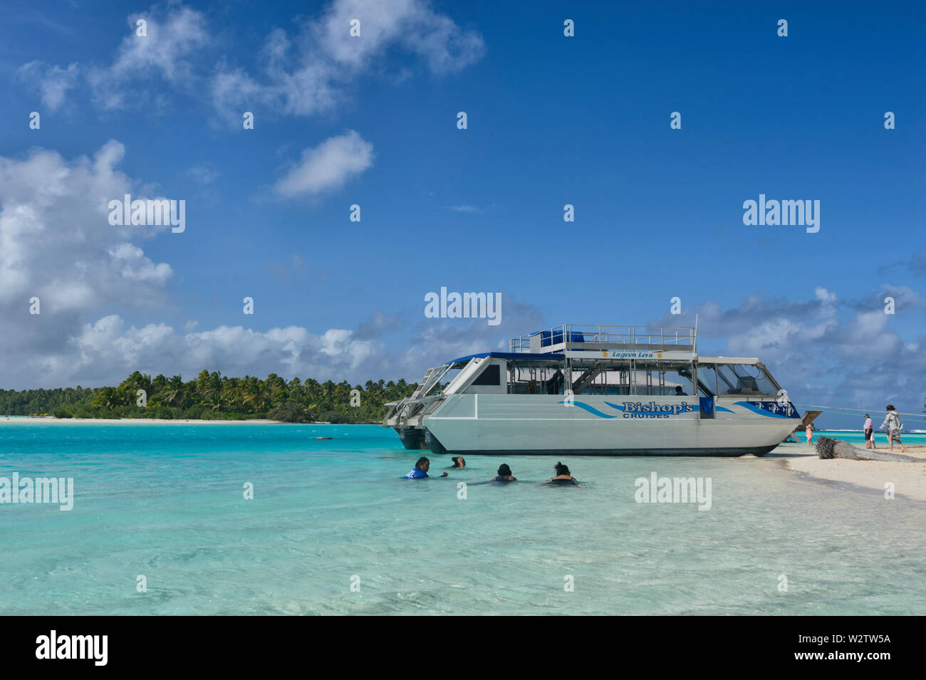 I turisti a nuotare in acque turchesi coral lagoon di Aitutaki davanti alla loro barca di crociera Isole Cook, Polinesia Foto Stock