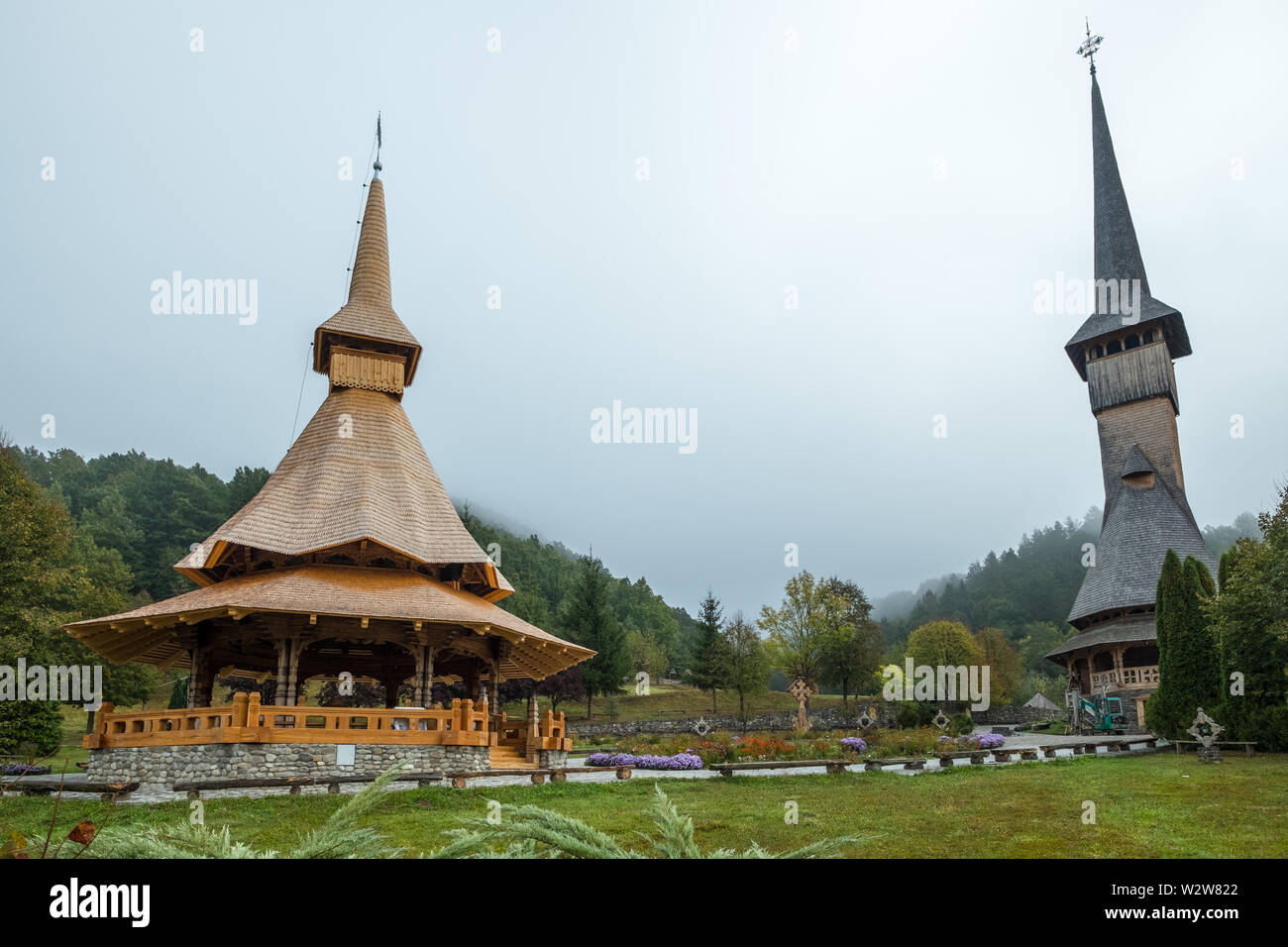 Iconici di legno alte guglie della chiesa e veranda situato in un giardino di Barsana Monastero, Maramures regione della Romania Foto Stock