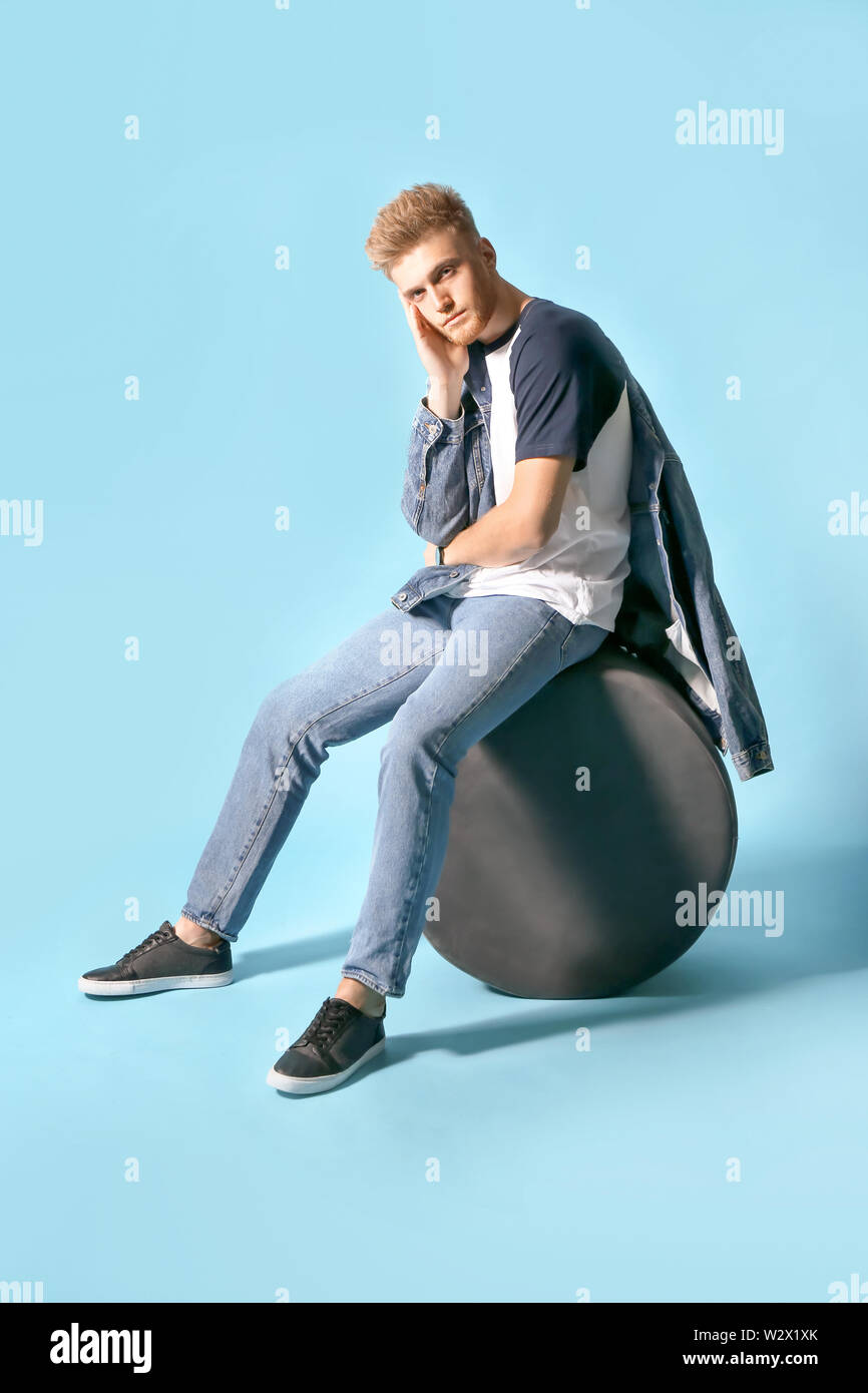 Elegante giovane uomo seduto sul pouf contro il colore di sfondo Foto Stock