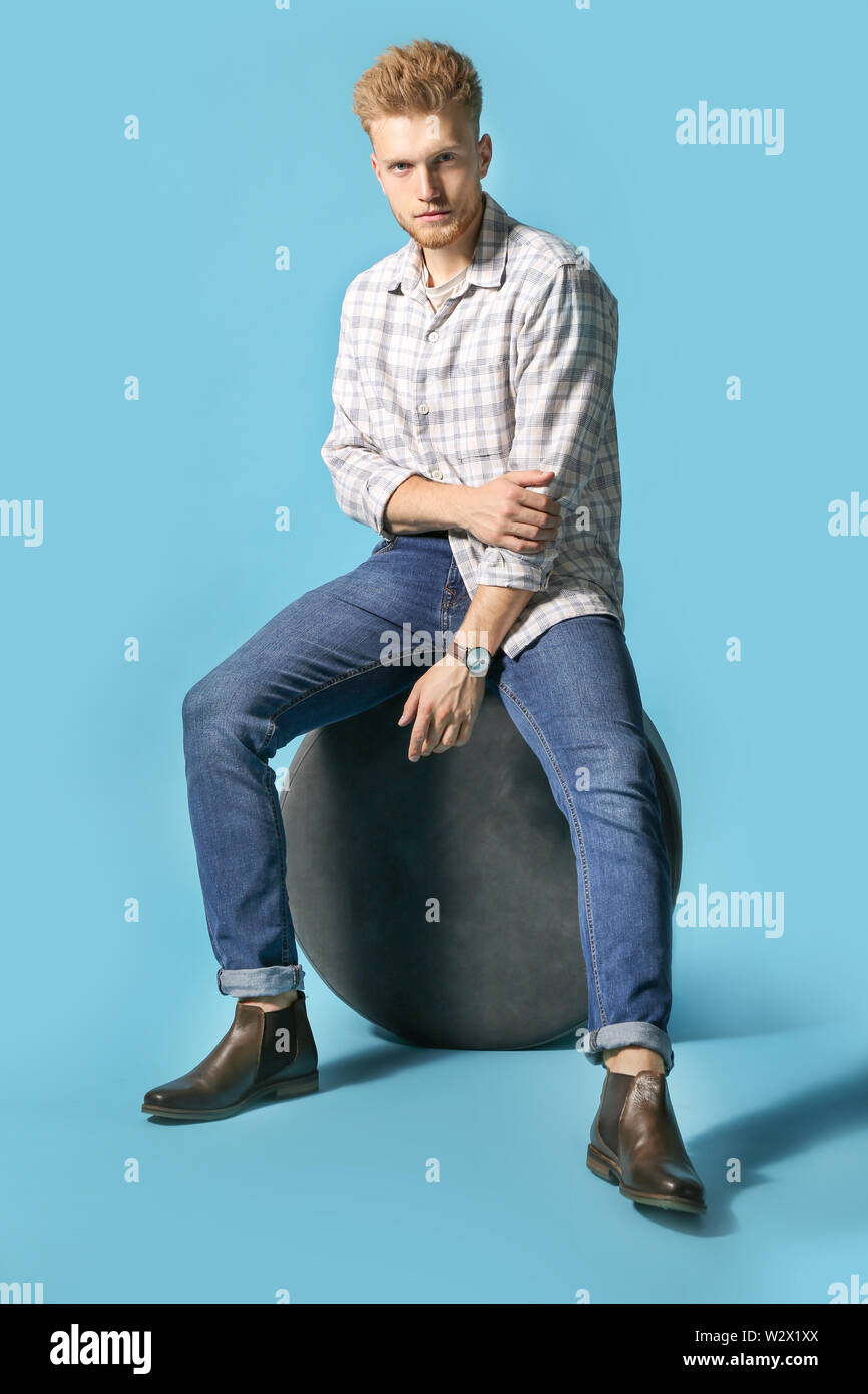 Elegante giovane uomo seduto sul pouf contro il colore di sfondo Foto Stock