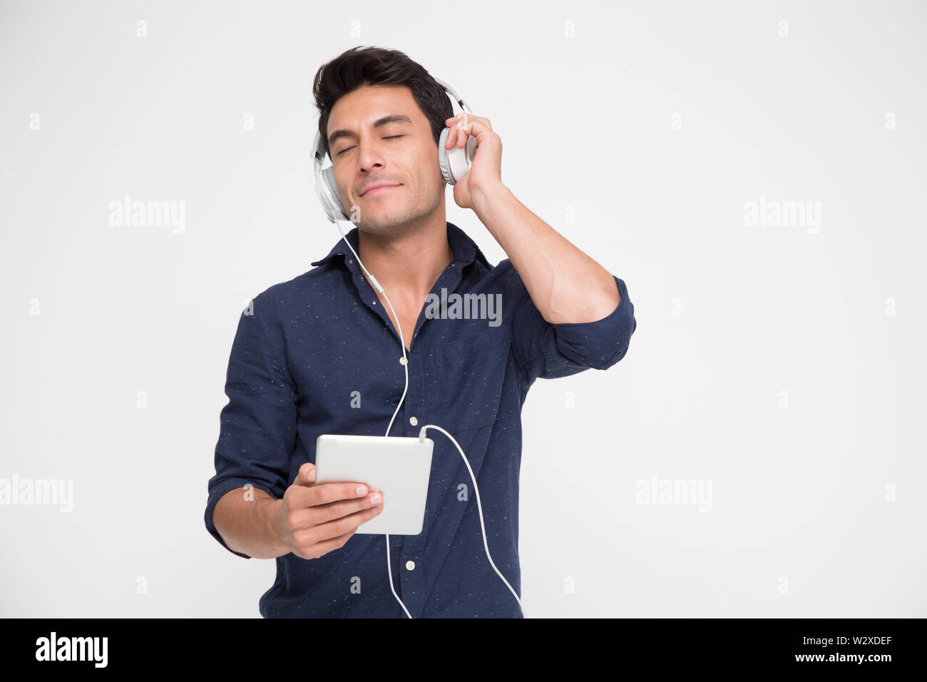 Bel giovane uomo caucasico ascoltando musica con le cuffie nel brano della playlist applicazione su tablet Foto Stock