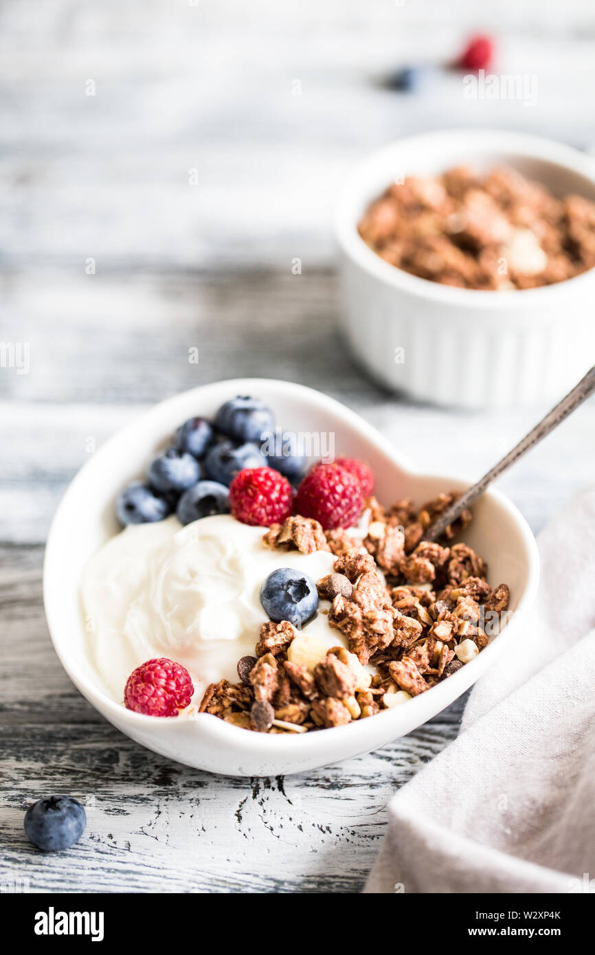 Lo yogurt greco, mirtilli e lamponi e granola in una ciotola bianco su uno sfondo di legno. Foto Stock