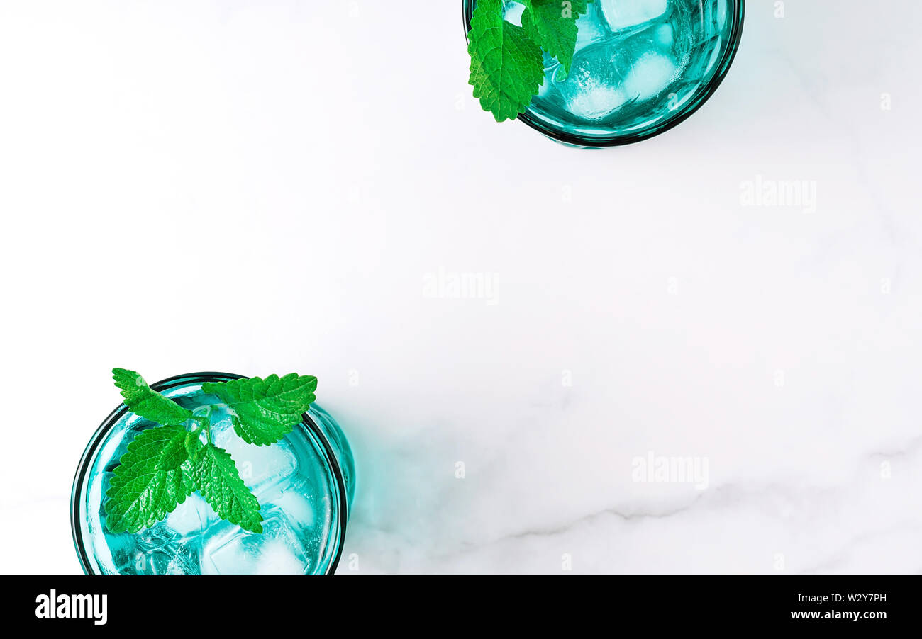 Due belle vintage occhiali turchese con bevanda fredda e cubetti di ghiaccio, decorata con fresco verde menta su marmo bianco tavola. Vista dall'alto. Foto Stock