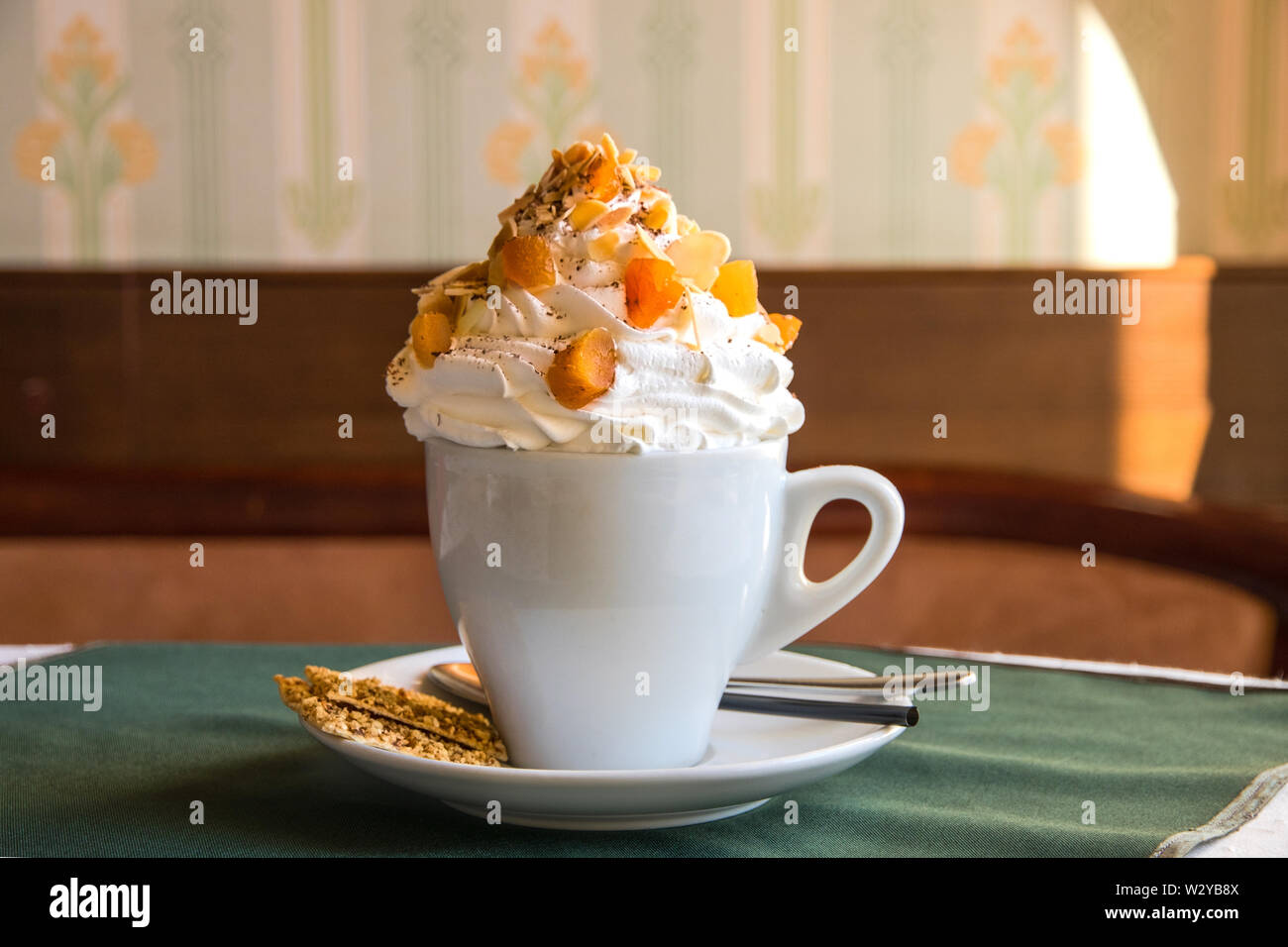 Caffè con panna montata e frutta secca in ceco bianco su un tavolo in un bar con un piccolo cookie su un piattino, cucchiaio e paglia. Deliziosi dessert in t Foto Stock