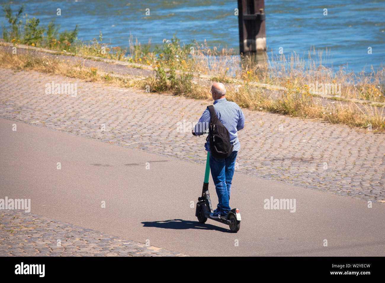 L'uomo su un affitto scooteron elettrico le rive del fiume Reno, Colonia, Germania. Mann auf Miet-Elektroscooter am Rheinufer, Koeln, Deutschland. Foto Stock