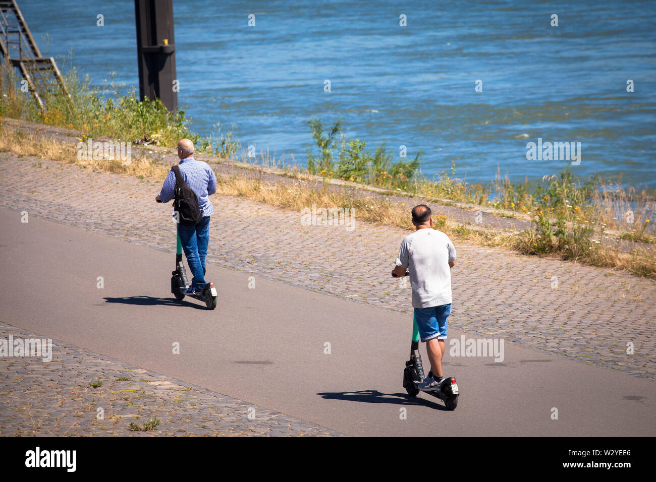 Gli uomini su un affitto scooteron elettrico le rive del fiume Reno, Colonia, Germania. Maenner auf Miet-Elektroscooter am Rheinufer, Koeln, Deutschland. Foto Stock