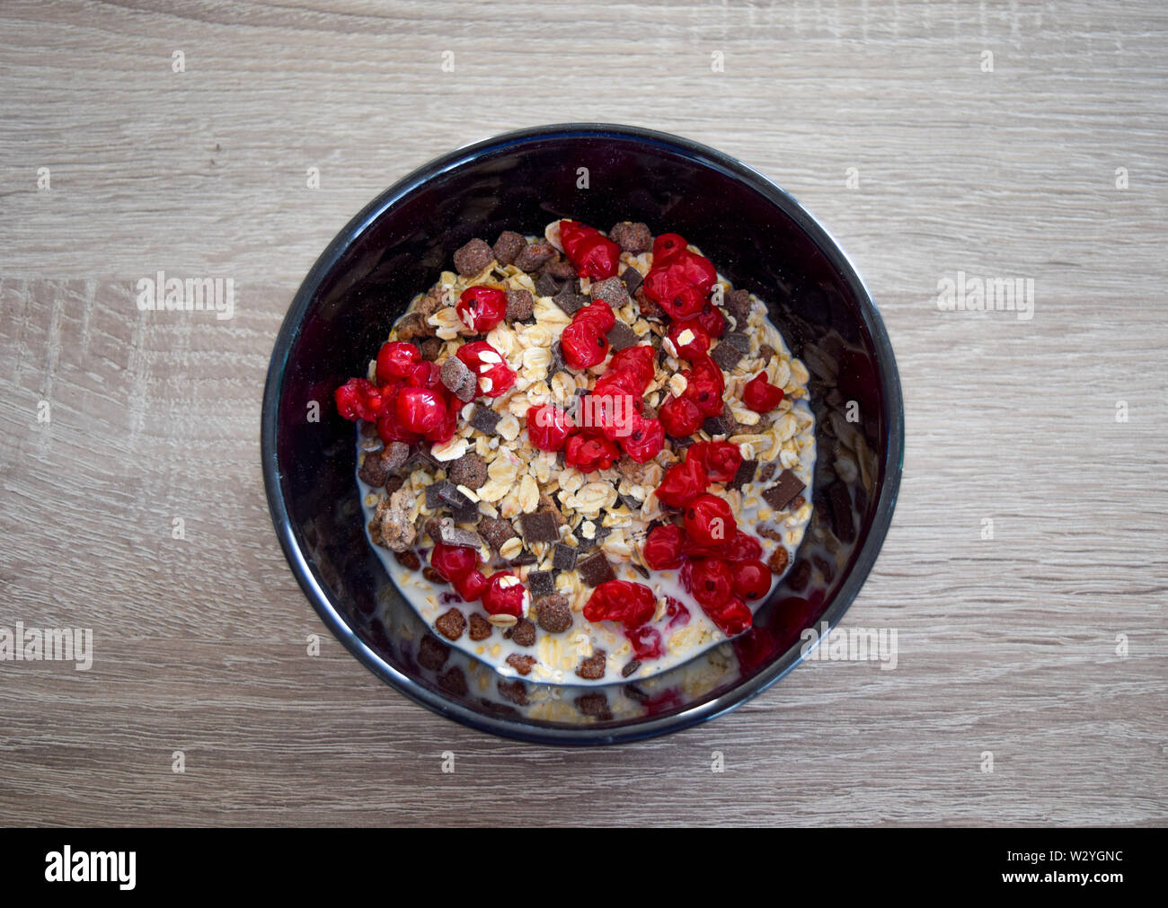 Farina di avena in una ciotola con freschi ribes rosso frutti di bosco, cioccolato e latte su un tavolo Foto Stock