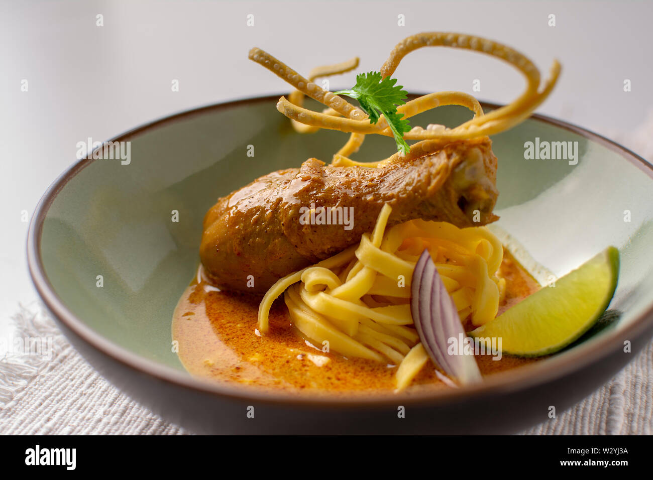 Thai giallo bacchette di pollo al curry con uova fresche tagliatelle , calce, coriandolo e croccante frittura di noodle all'uovo in un piatto placcato Foto Stock