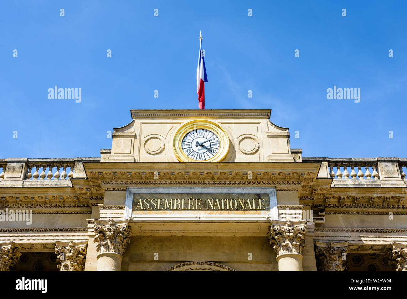 Close-up di Frontone con orologio e bandiera dell'entrata sud del Palais Bourbon, sede dell'Assemblea nazionale francese a Parigi, Francia. Foto Stock