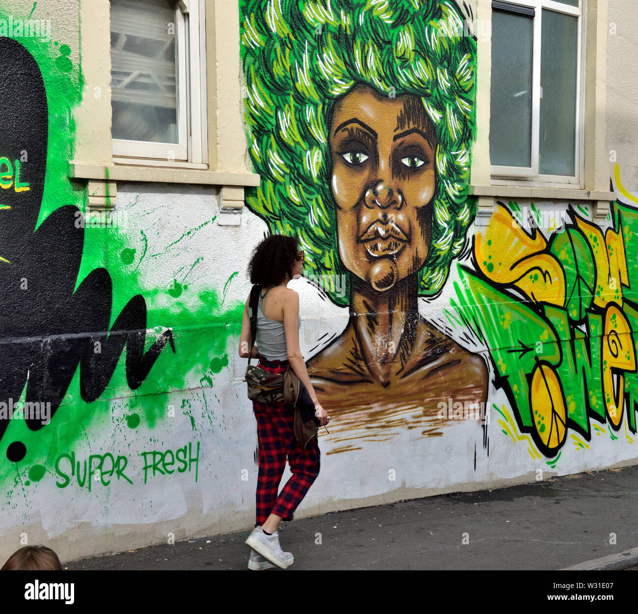 La donna a piedi oltre la parete con graffiti wall art in san Paolo Bristol durante il carnevale locale Foto Stock