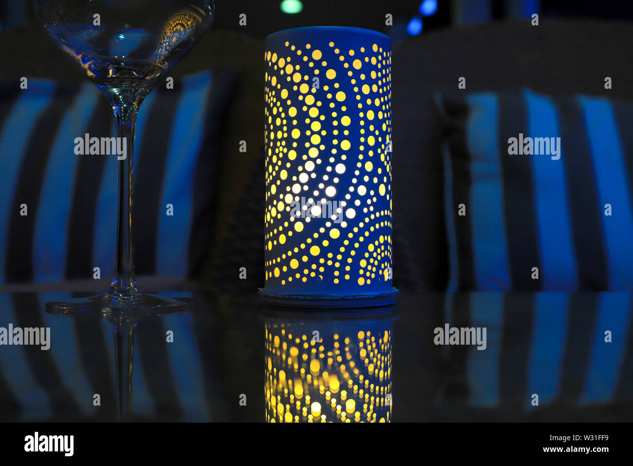 La Lampada sul tavolo vacanze in serata cena. Elegante lanterna blu con una candela gialla su un tavolo in vetro e un bicchiere di notte. Foto Stock