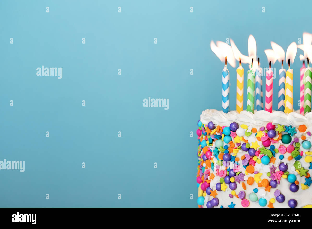 Torta di compleanno con un sacco di candele colorate e spruzza su uno sfondo blu Foto Stock