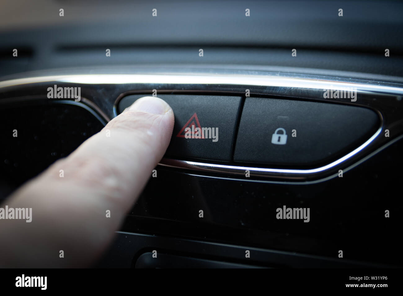 Un dito che preme le luci di avvertimento pericolo su un auto interno Foto Stock