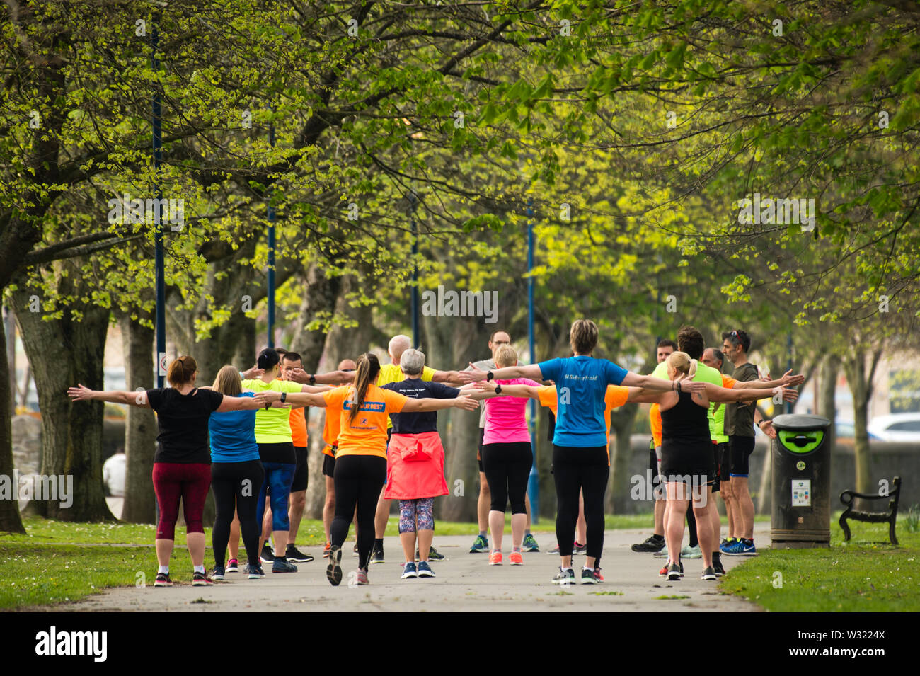 Adulti per tenersi in forma : un gruppo pf persone in luminoso fluorescente lycra in esecuzione esercizio jogging all'aperto nel parco in una calda serata primaverile, Aberystwyth Wales UK Foto Stock