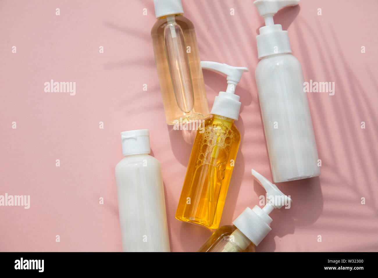 I prodotti cosmetici in bottiglie su uno sfondo rosa con tropical di foglie di palma ombra Foto Stock