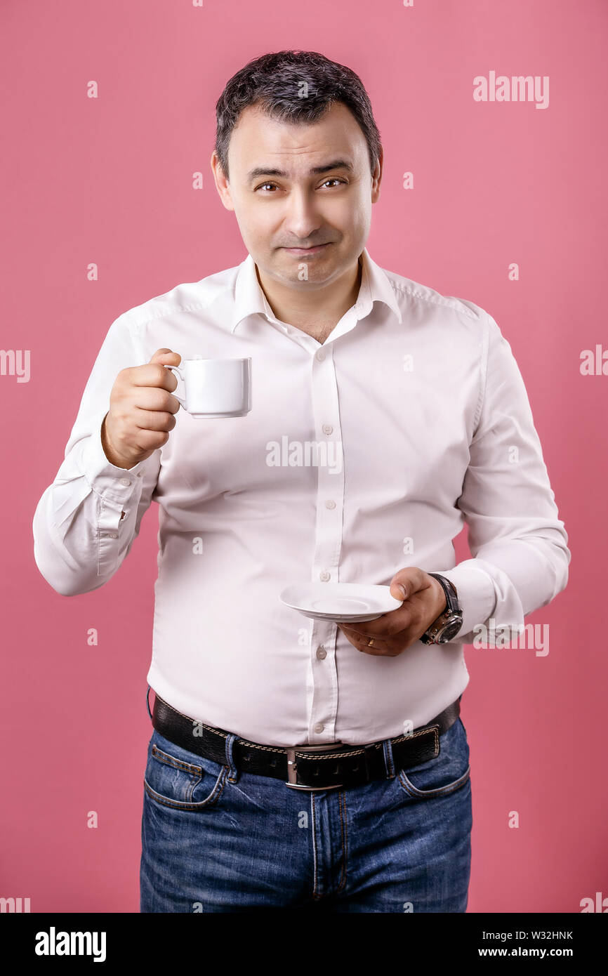 Sorridente uomo adulto con tazza di caffè guardando la telecamera contro isolate di sfondo rosa. Foto Stock