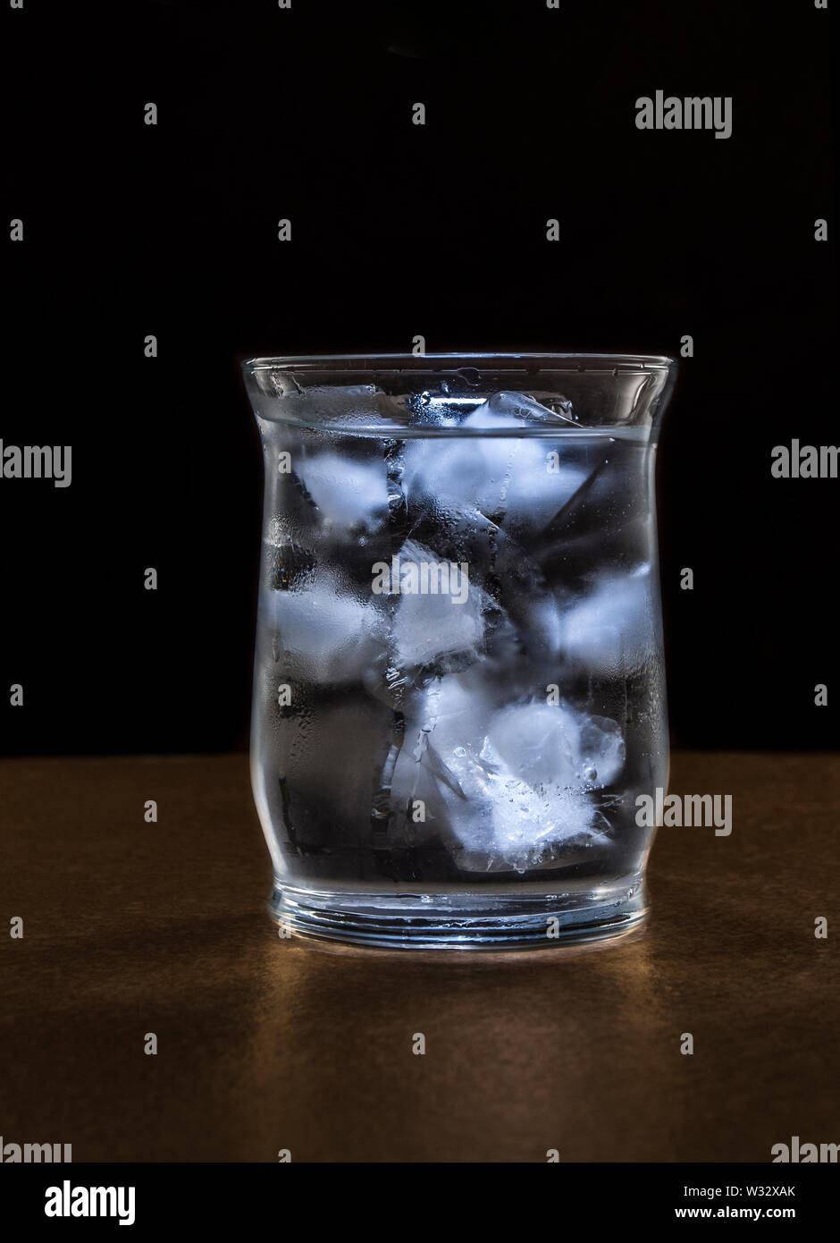 Un bicchiere di acqua con ghiaccio in un ambiente oscuro, bassa luce chiave fotografia Foto Stock