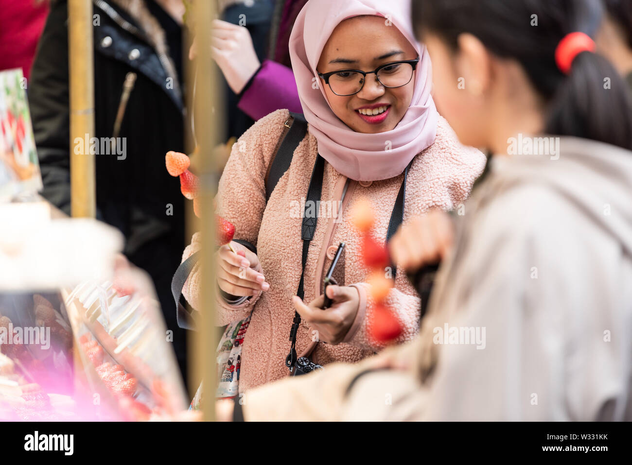 Tokyo, Giappone - 30 Marzo 2019: popoli asiatici e donna musulmana acquisto di spiedini di fragole dal fornitore giapponese in store Ginza Tsukiji street fis esterno Foto Stock