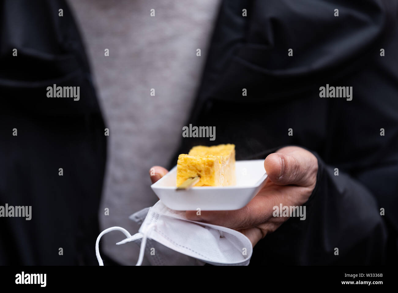 Primo piano della persona mani tamagoyaki giapponese uova frittata arrotolata in Ginza del pesce di Tsukiji street mercato esterno con nessuno Foto Stock